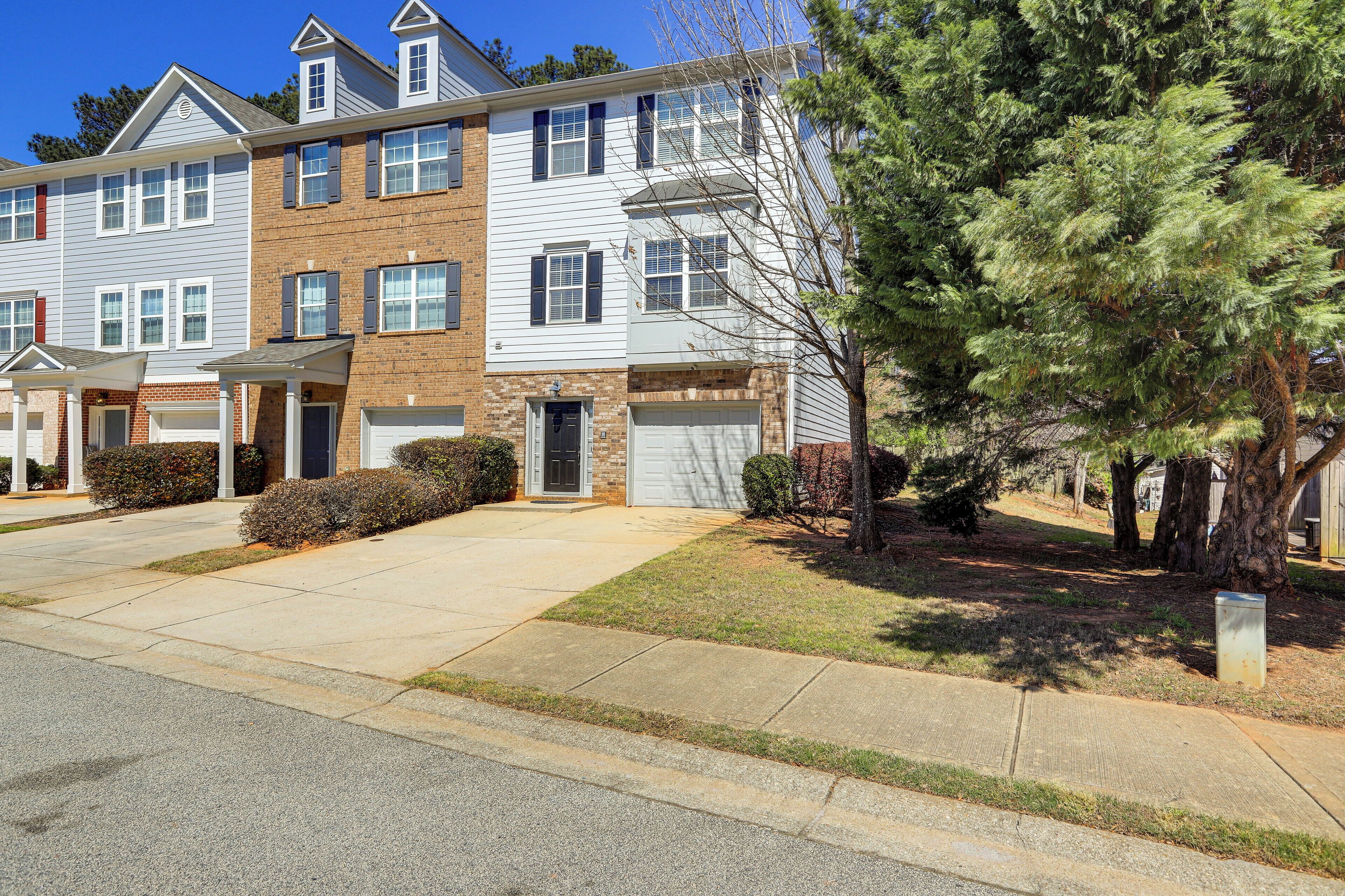 A multi-story residential building with a front garage, a covered driveway, and a well-maintained lawn.