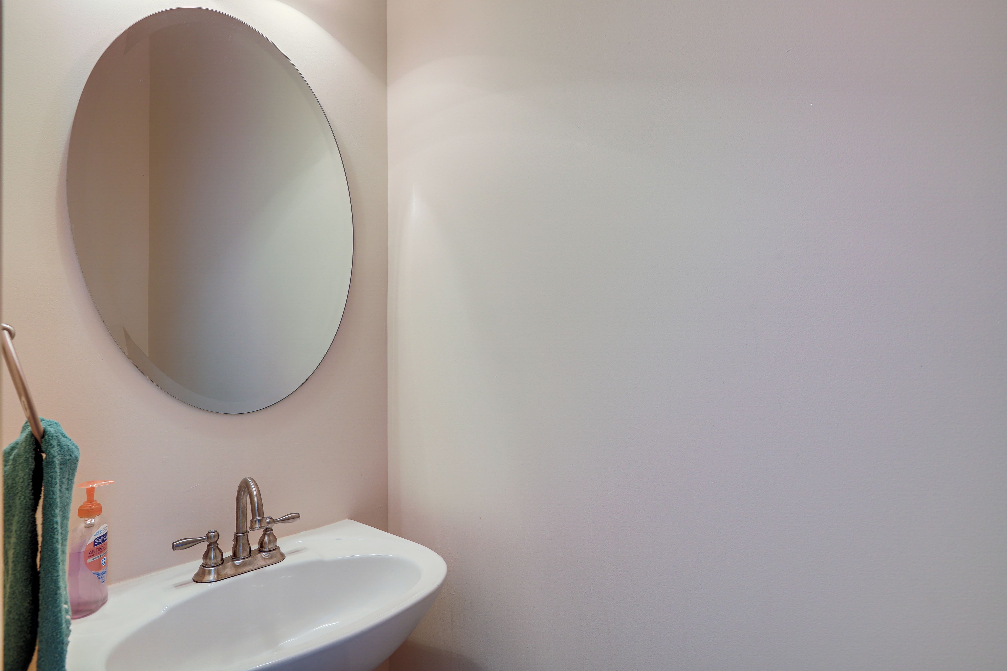 Une salle de bain avec un lavabo blanc, un miroir rond et une serviette suspendue à un porte-serviettes.