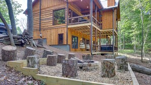 Une cabane en bois dotée d’une terrasse, d’un foyer et d’une pile de bûches.