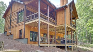 Une cabane en bois à deux étages, dotée d’un balcon, de grandes fenêtres et surplombant une forêt.