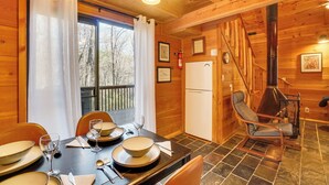 Ein Holzblockhaus-Innenraum mit einem Esstisch, der für vier Personen gedeckt ist, einem Stuhl, einem Herd und einem Kühlschrank.