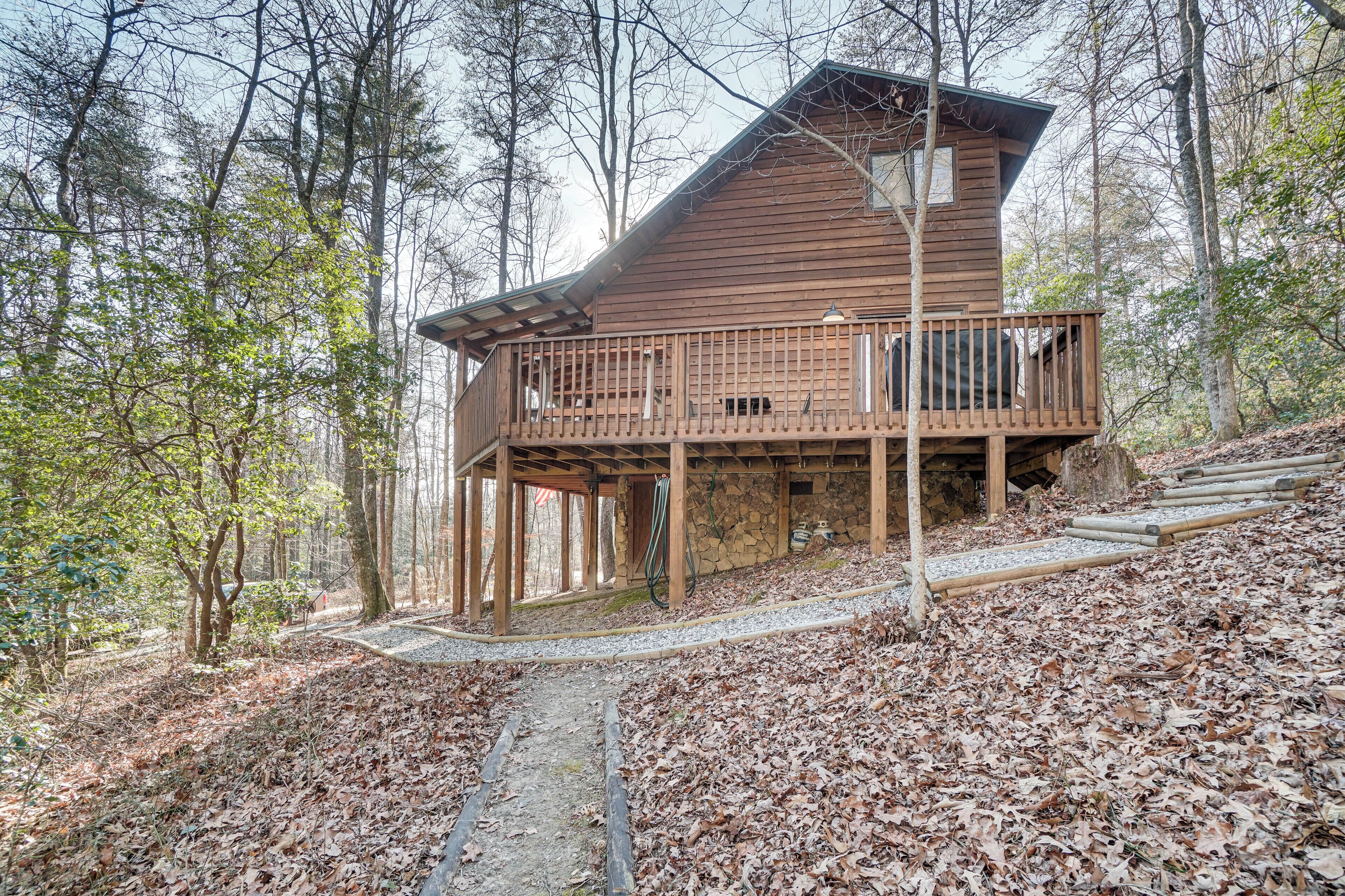 Une cabane en bois dotée d’un balcon, entourée d’arbres et bordée d’un chemin de gravier.