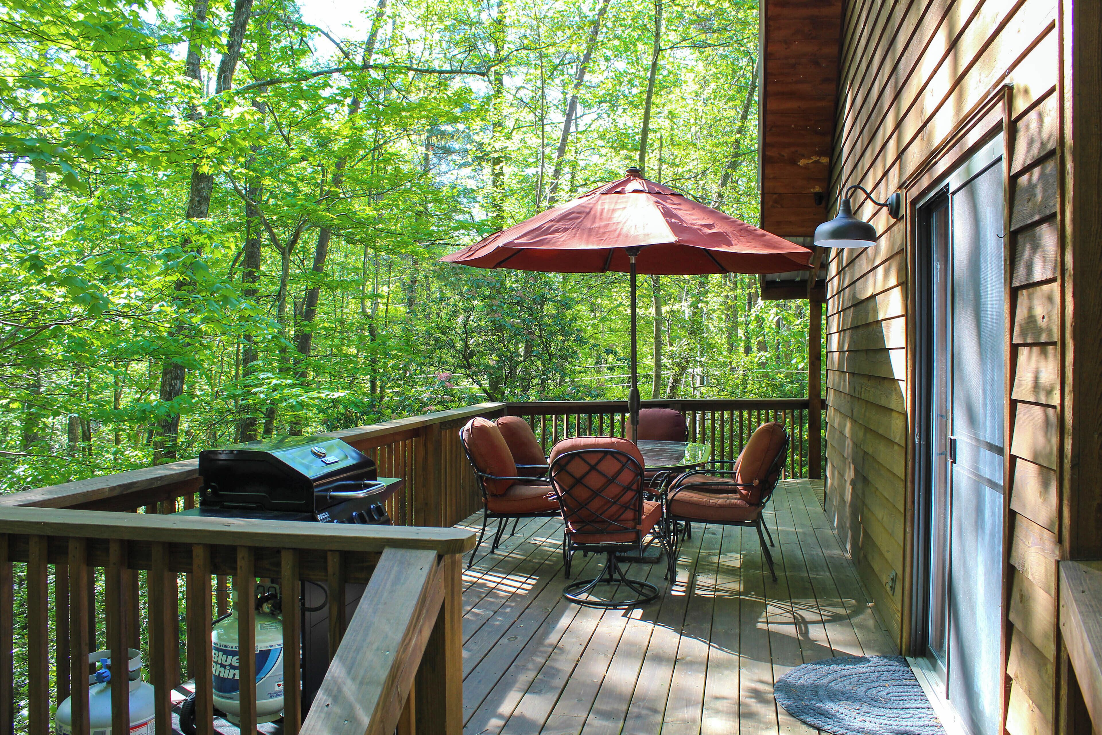 A wooden deck with outdoor furniture, a grill, and a large umbrella.