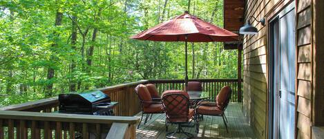 A wooden deck with outdoor furniture, a grill, and a large umbrella.