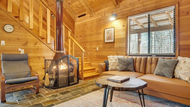 Ein gemütliches Blockhauskabinen-Interieur mit Kamin, einer Couch, einem Sessel und einer Treppe.