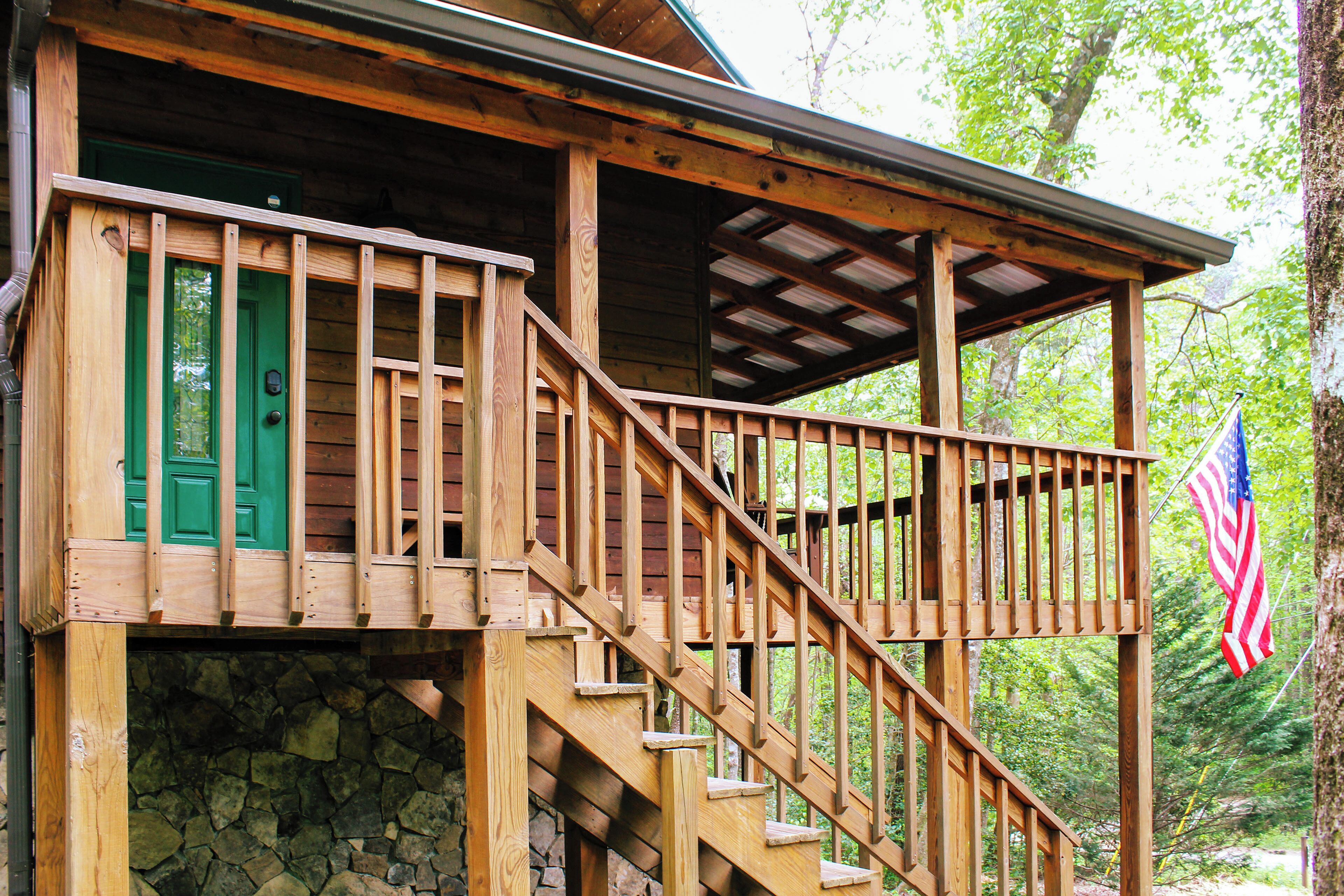 A wooden cabin with a stone foundation, a green door, and a wooden staircase leading to a covered porch.