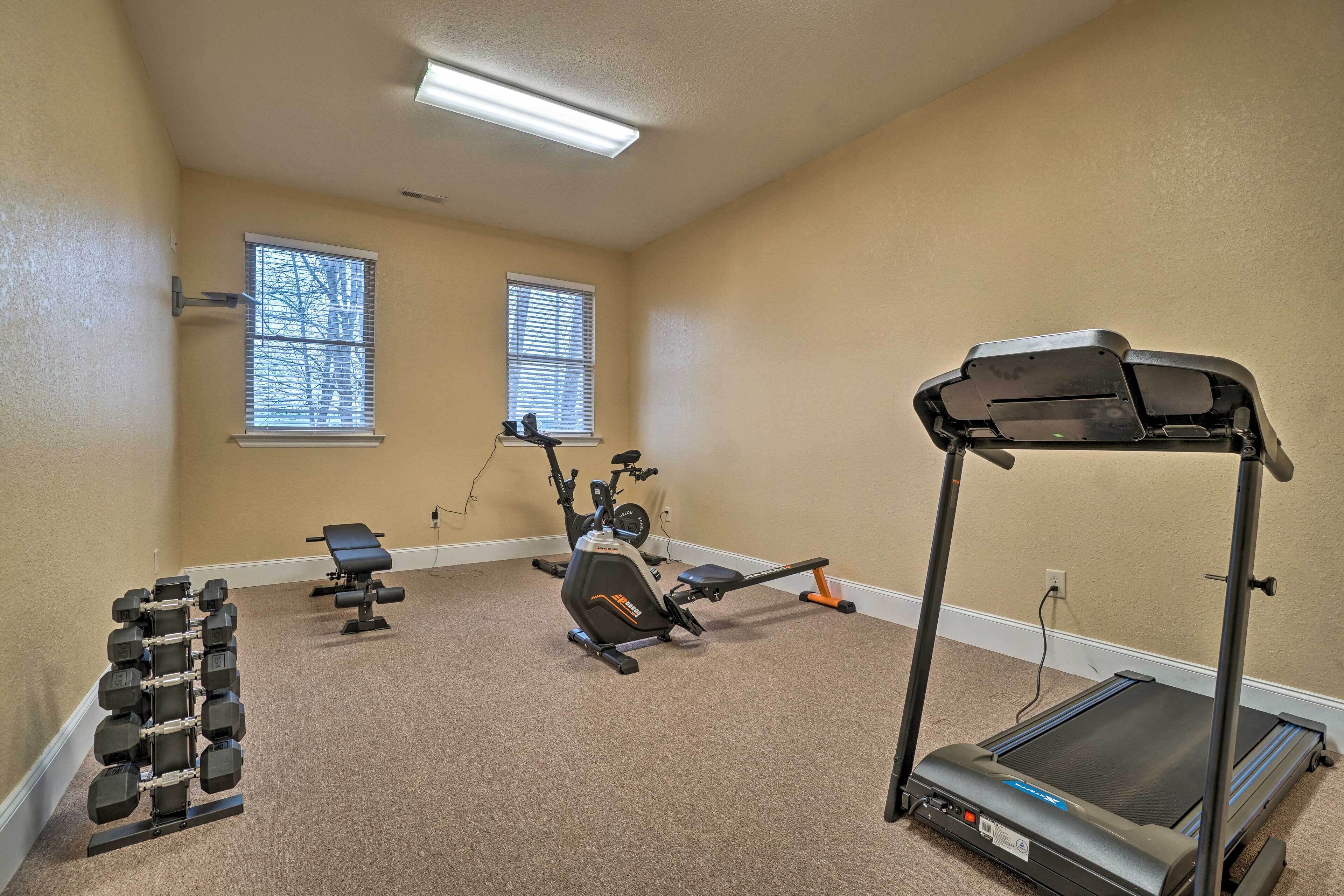 A home gym with a treadmill, stationary bike, dumbbells, and a bench.