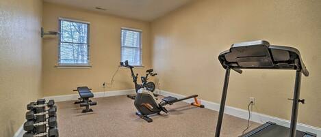 A home gym with a treadmill, stationary bike, dumbbells, and a bench.