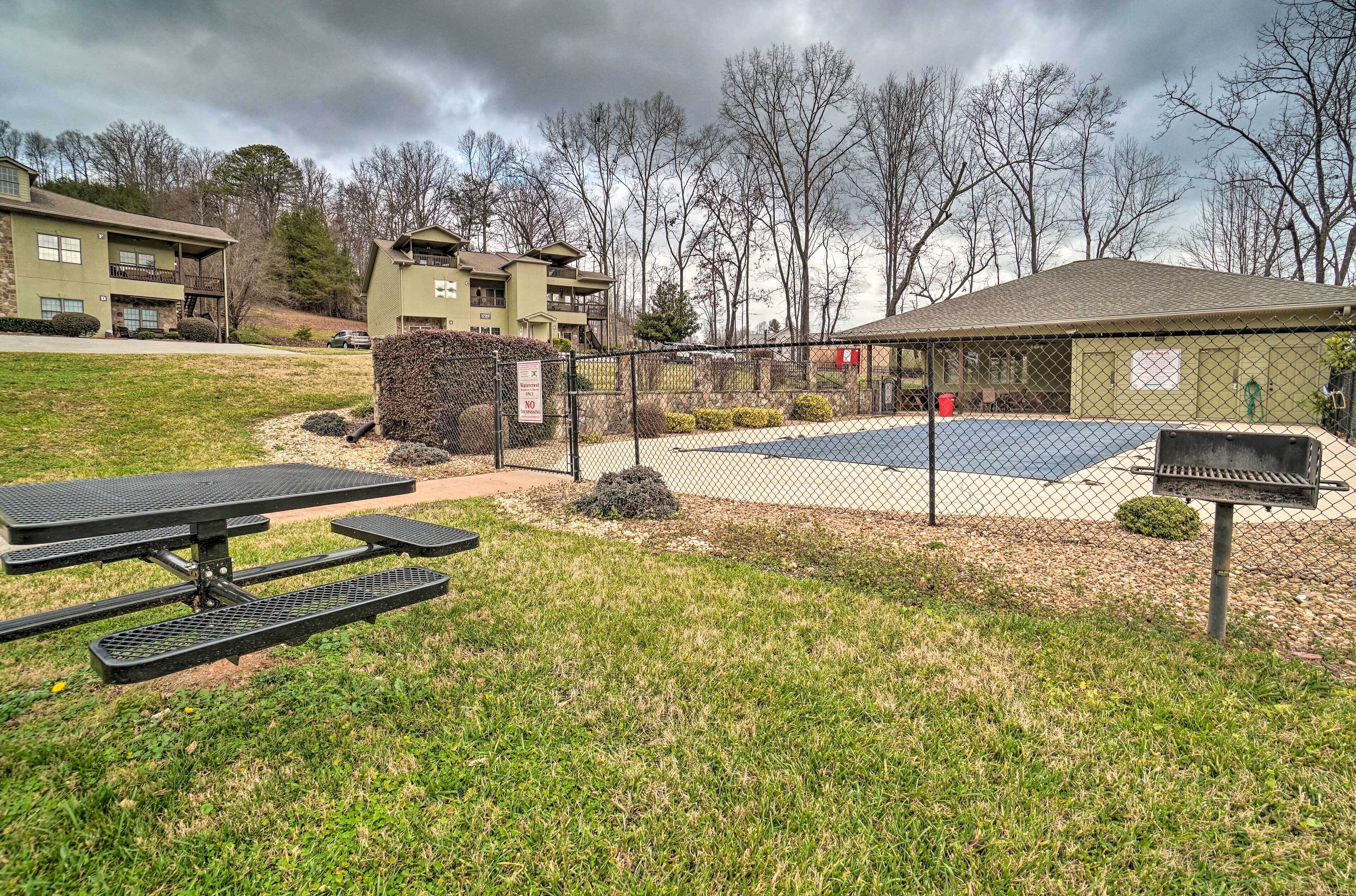 A fenced outdoor area with a picnic table, a barbecue grill, and a basketball court.