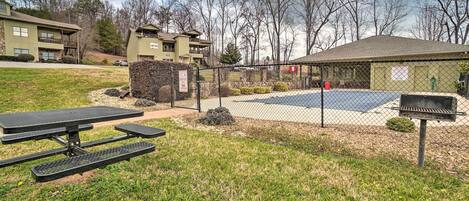 A fenced outdoor area with a picnic table, a barbecue grill, and a basketball court.