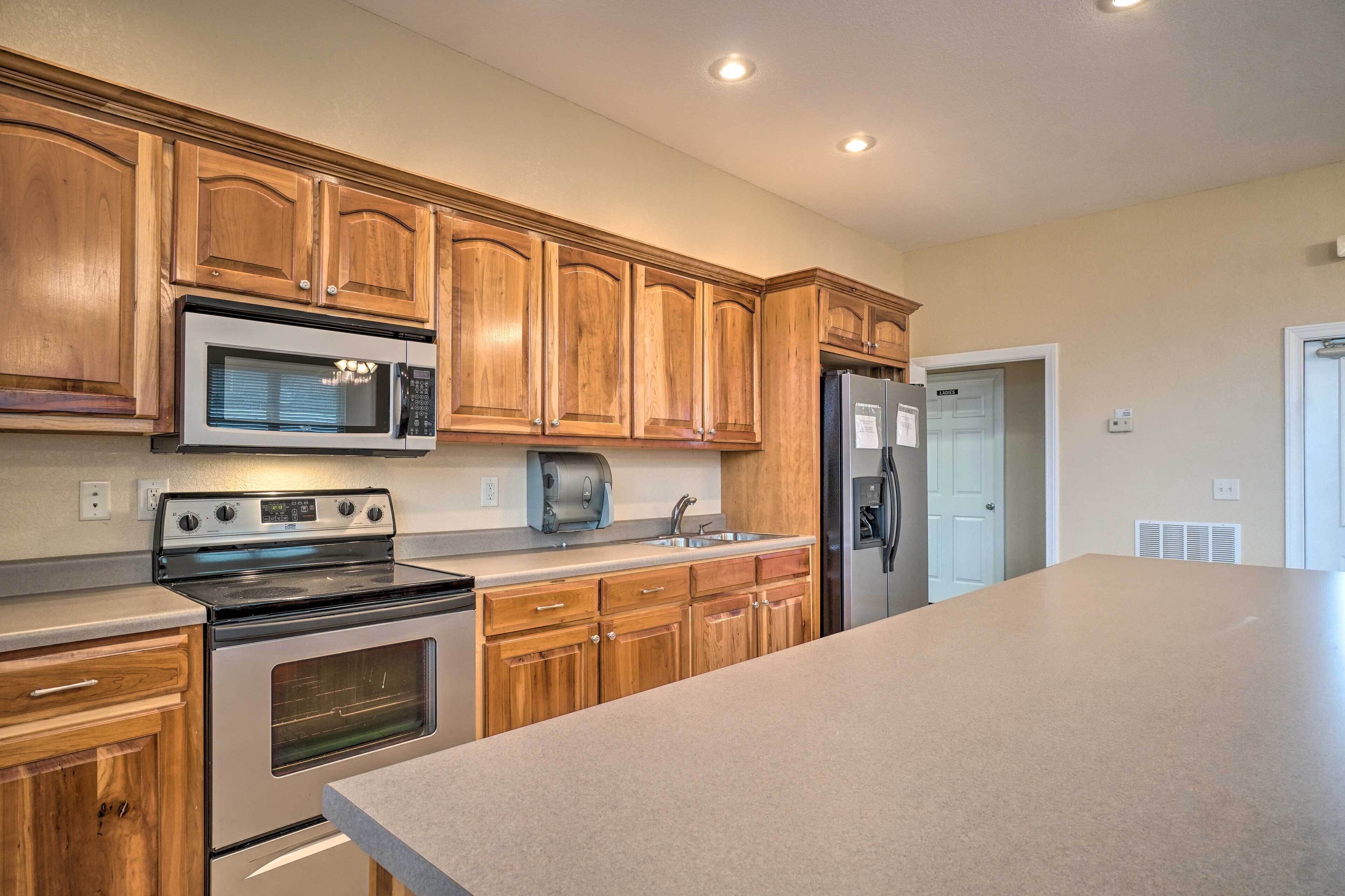 A kitchen with wooden cabinets, a stainless steel microwave, a built-in oven, a refrigerator, and a large countertop.