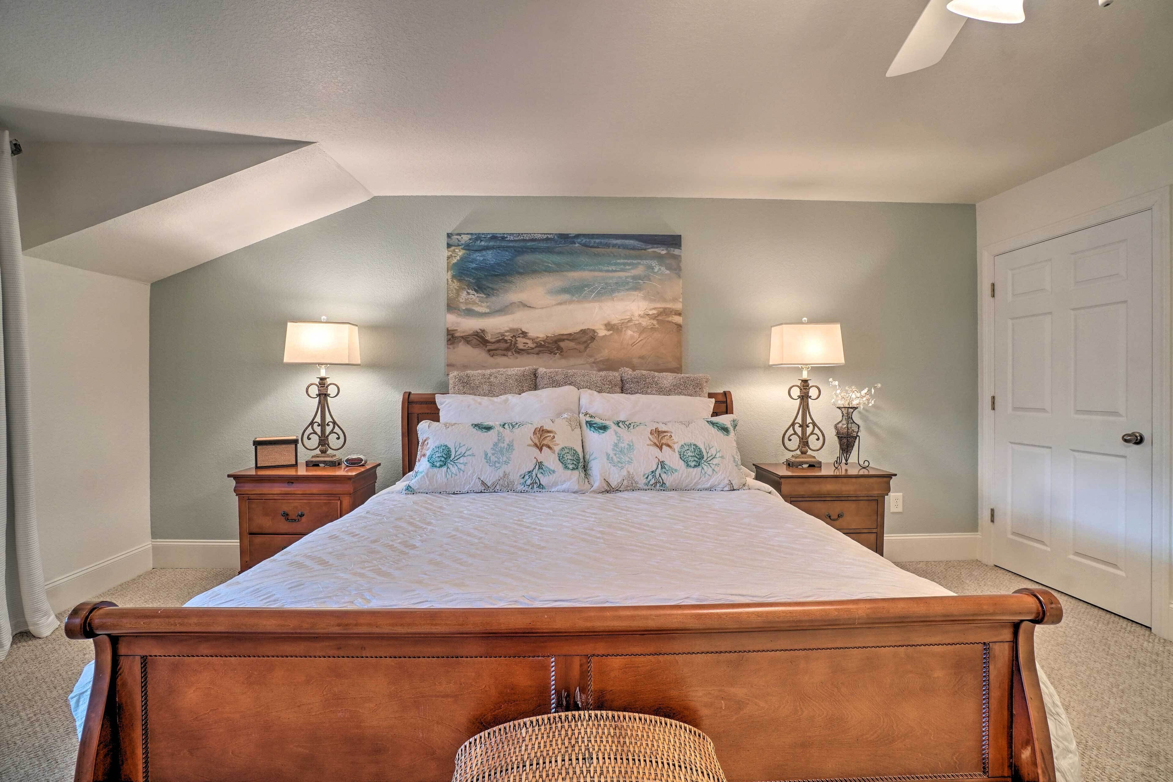 A bedroom with a wooden bed, two bedside tables with lamps, a wall-mounted painting, and a door.