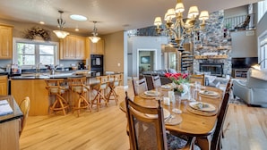 A spacious kitchen with wooden cabinets, a large island with bar stools, and a dining area with a wooden table set for four. - Sky Valley Home w/ Mtn View, 5 Mi to Rabun Bald! (Dillard)