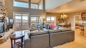 A spacious living area with a large sectional sofa, a stone fireplace, and a dining area with a chandelier. - Sky Valley Home w/ Mtn View, 5 Mi to Rabun Bald! (Dillard)