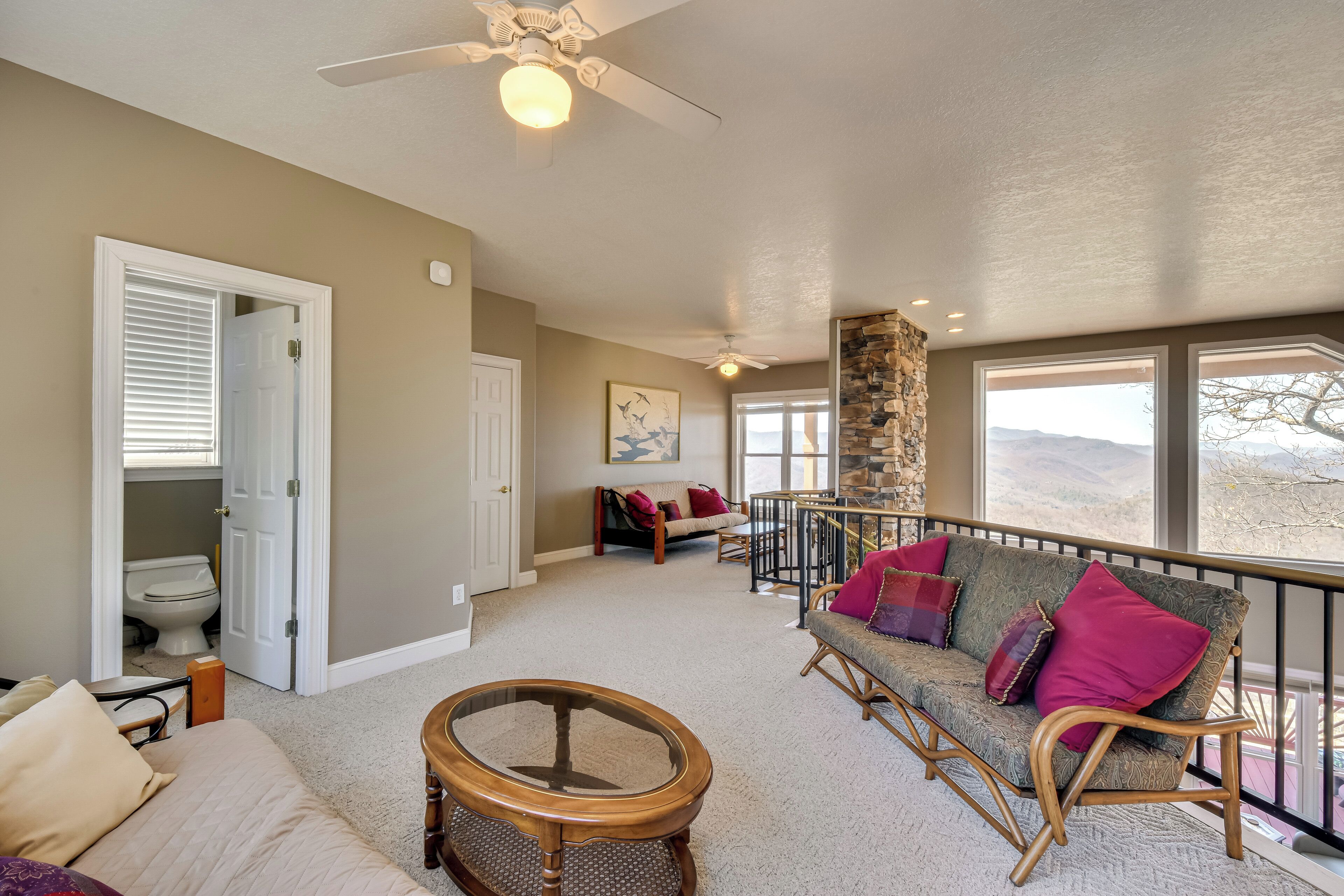 A spacious living area with a balcony, a sofa with cushions, a round wooden table, and a ceiling fan.