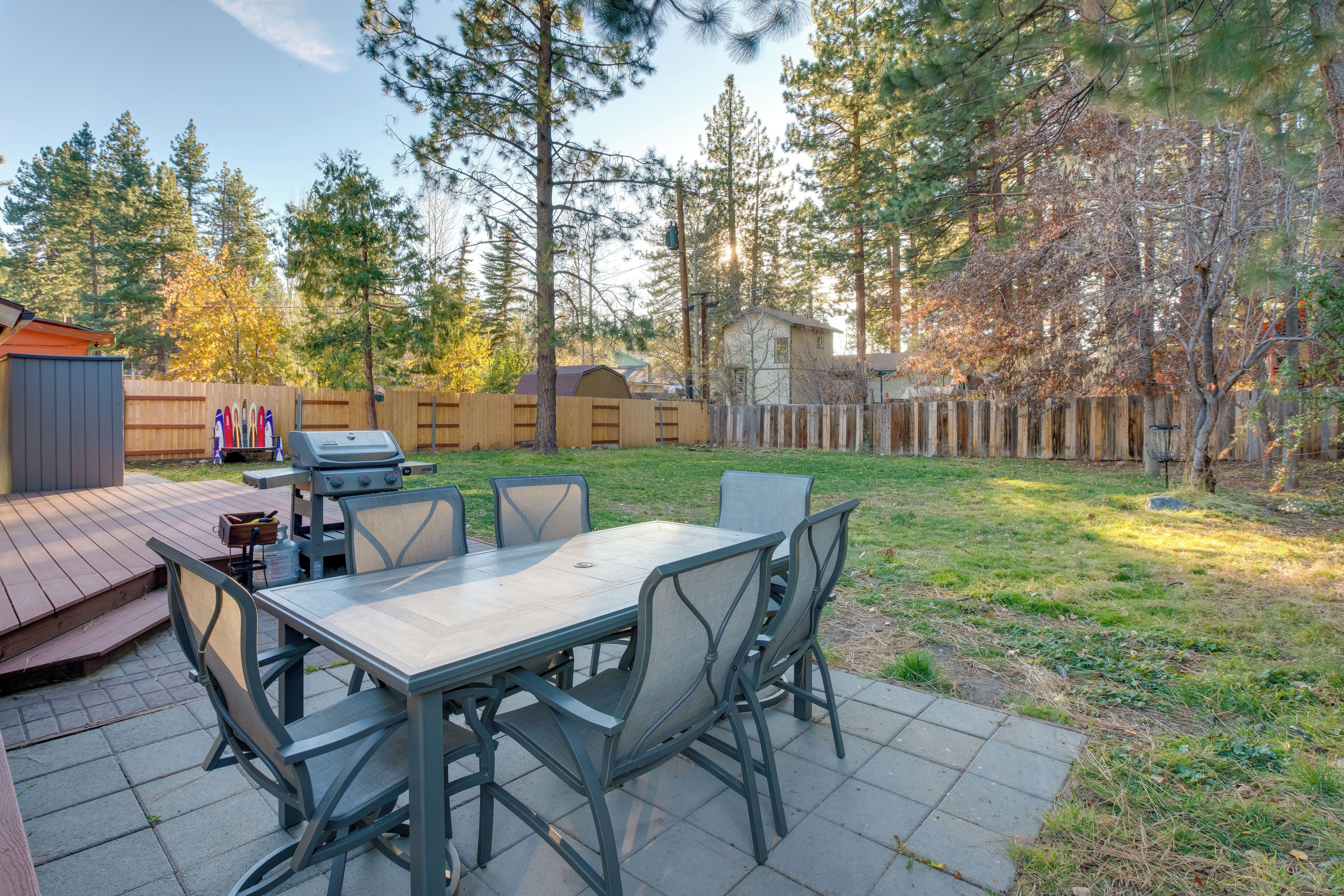A backyard with a wooden deck, a barbecue grill, and a dining table with chairs.