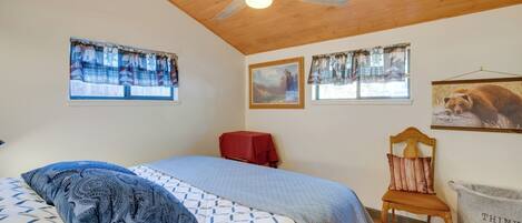 A bedroom with a bed, a wooden ceiling fan, a red chair, and a wall-mounted trash bin.