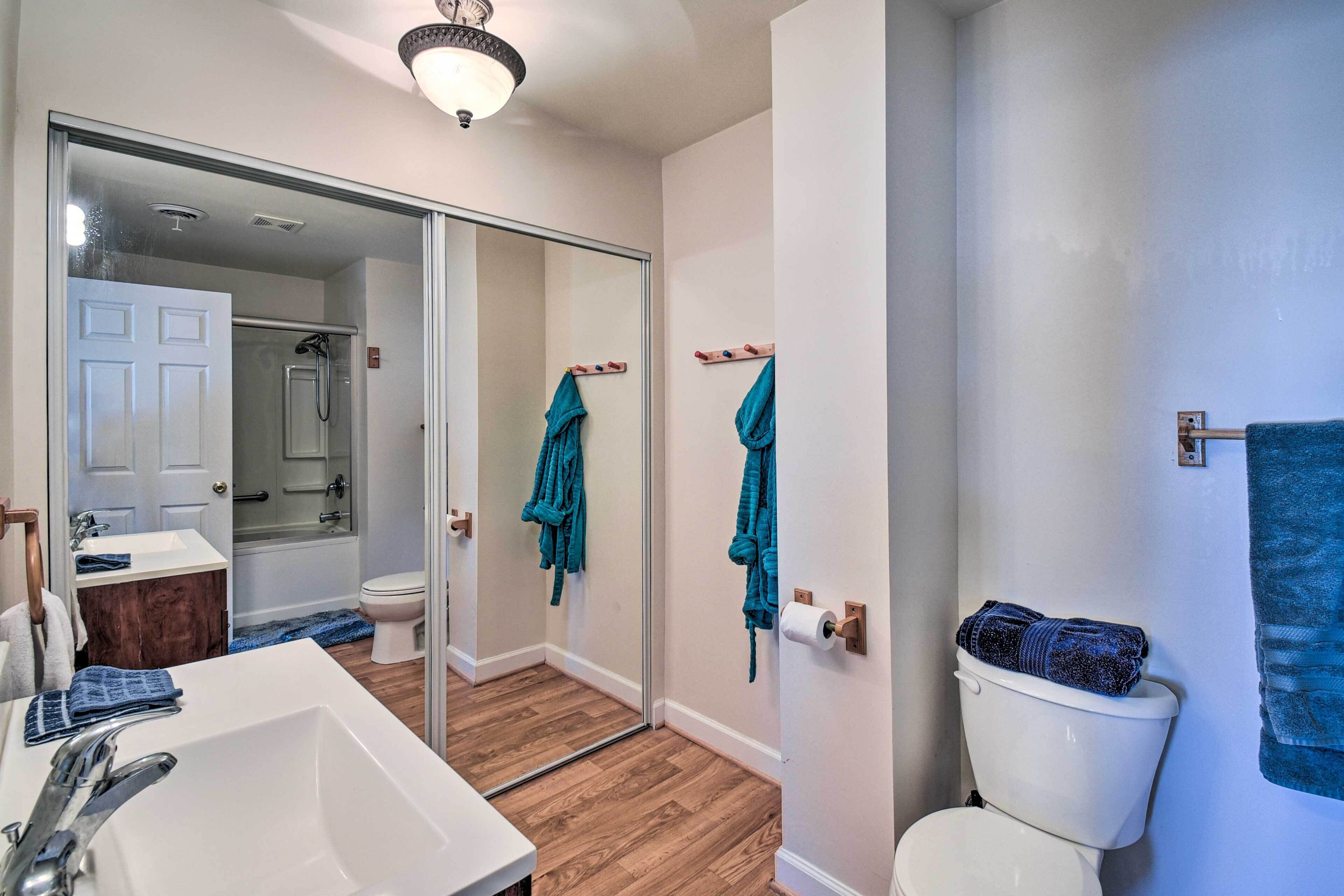 A bathroom with a white sink, a toilet, and a shower. There are towels hanging on hooks and a mirror.