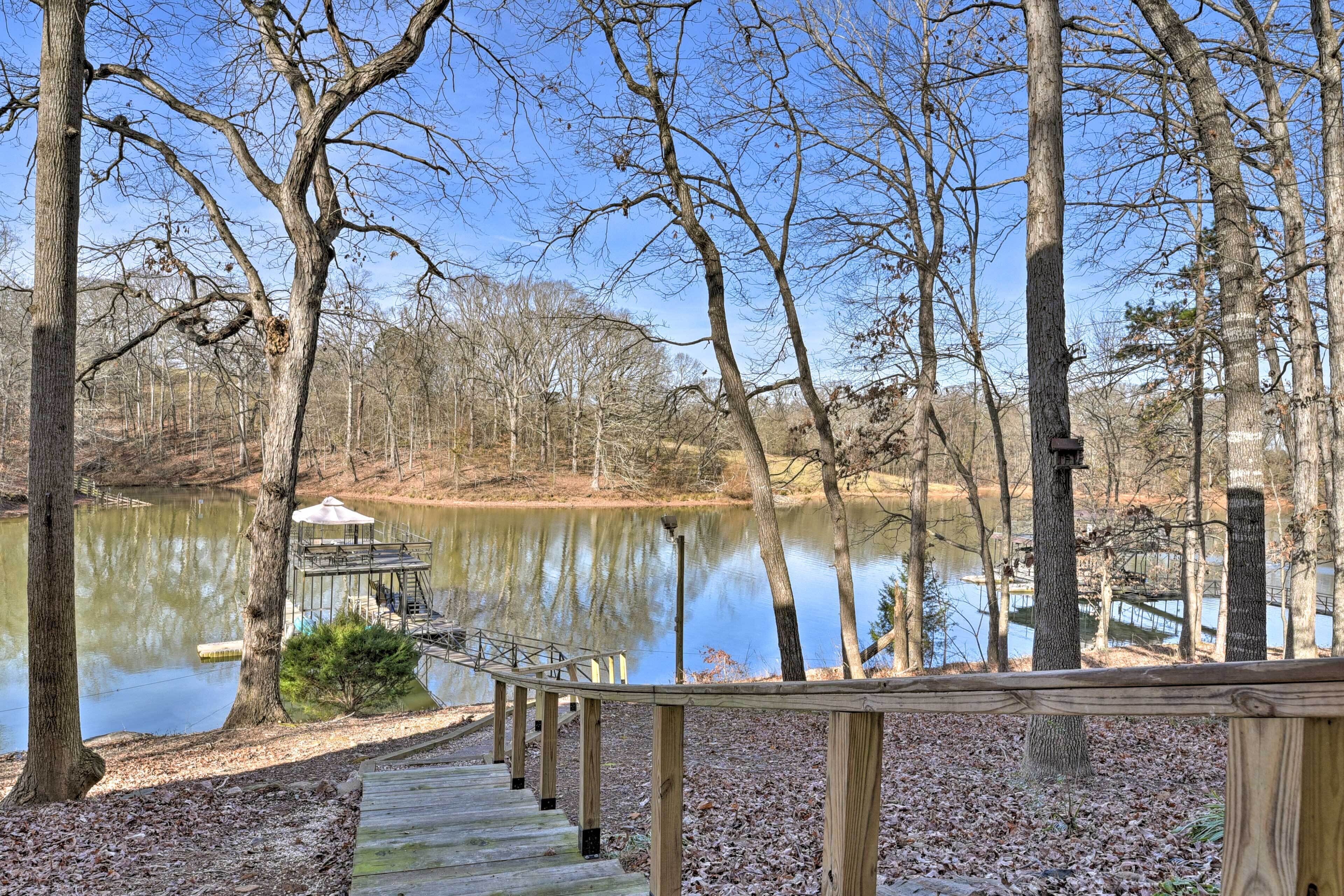 A wooden deck leading to a lake with a gazebo and a bird feeder.