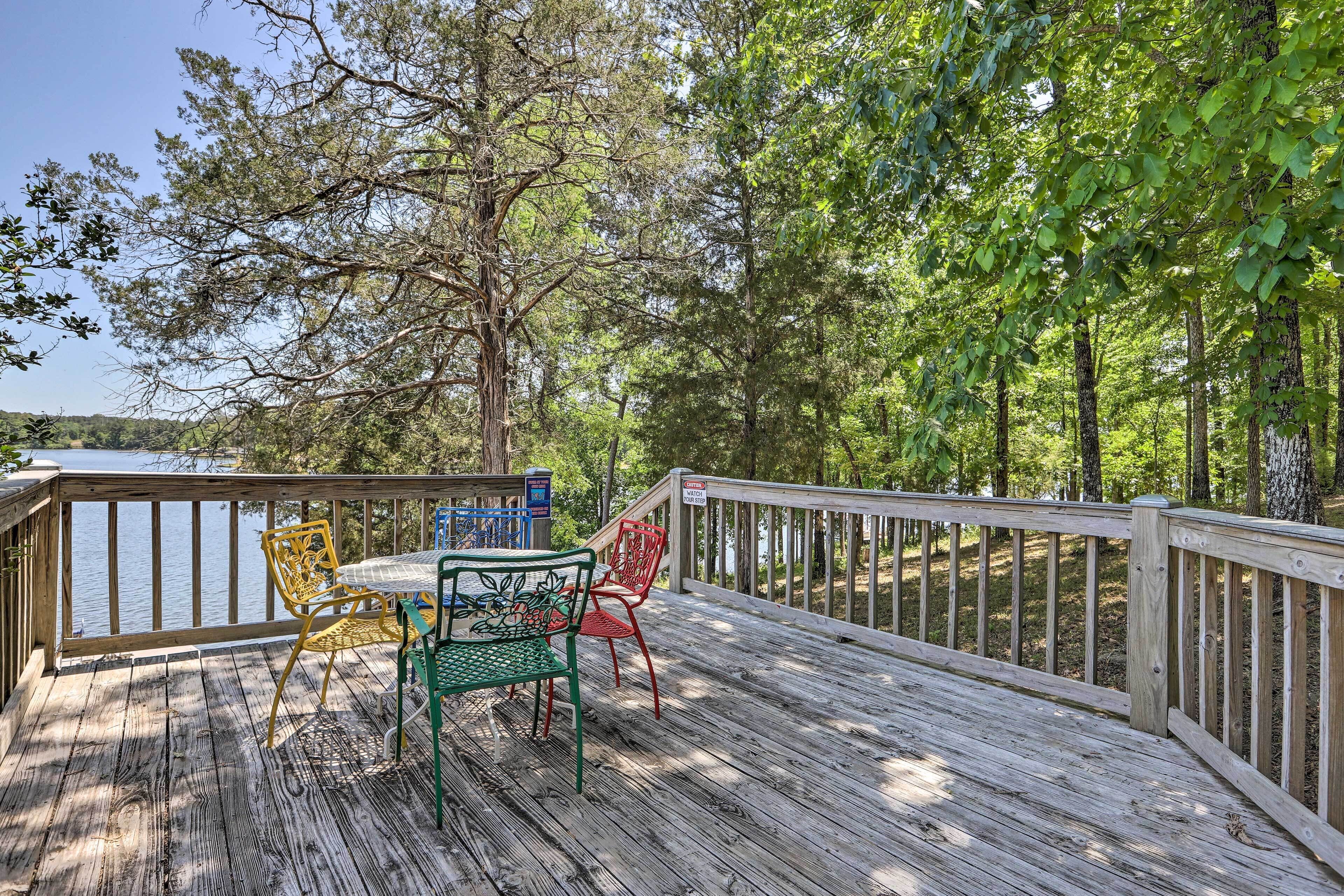 A wooden deck with a table and chairs, overlooking a body of water and surrounded by trees.