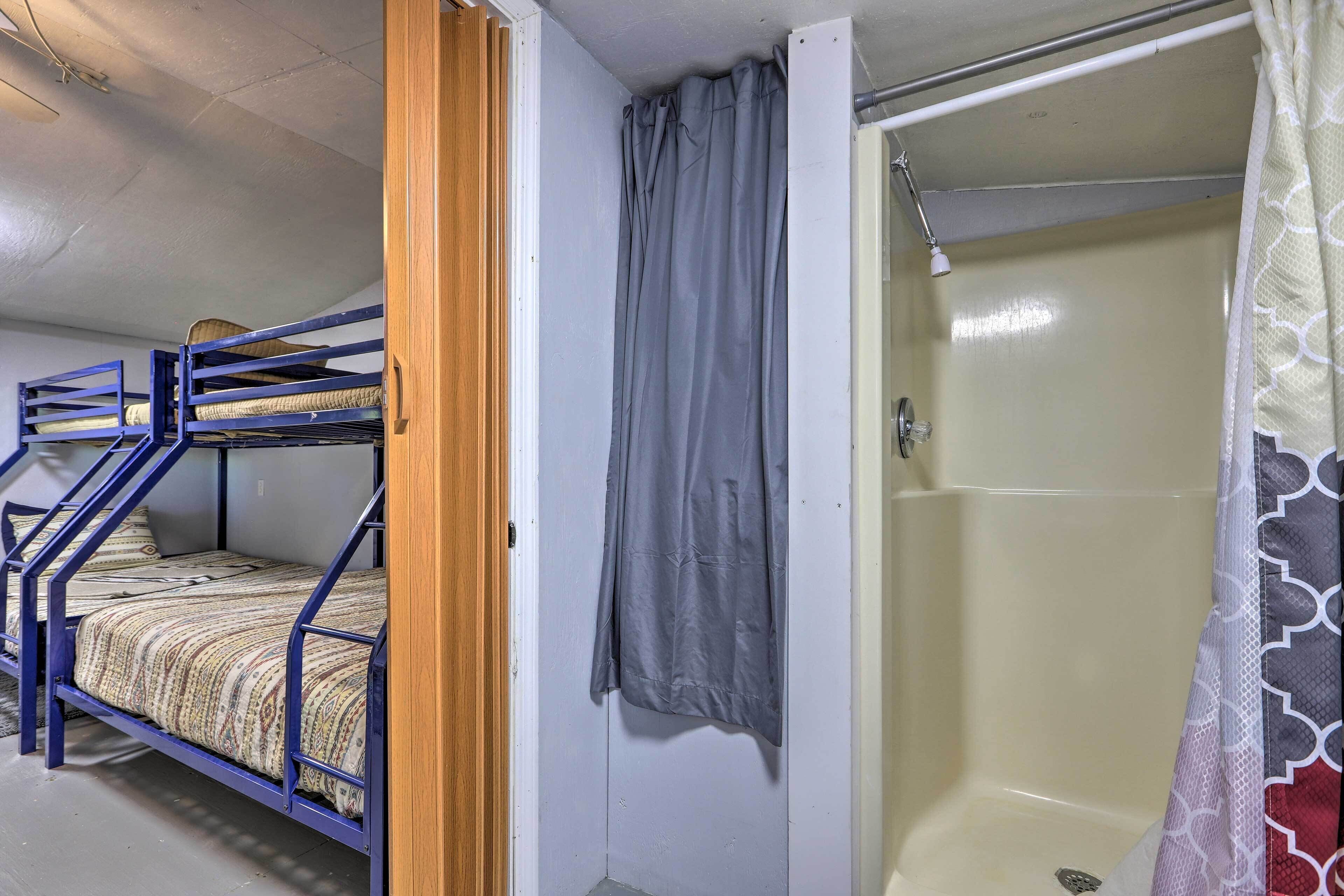 A bunk bed with a wooden door, a shower with a grey curtain, and a patterned shower curtain.