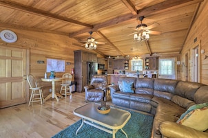 A spacious living room with a large leather sectional sofa, a dining table with chairs, and a kitchen area in the background.