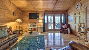 L’intérieur chaleureux d’un chalet avec un plafond en bois, un salon comprenant un canapé, une table basse et un téléviseur.