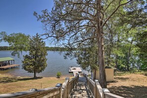 A wooden deck leading to a dock over water, surrounded by trees and a small building. - House w/ Dock + Slide Situated on Lake Sinclair! (Milledgeville)