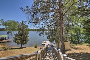 A wooden deck leading to a dock over water, surrounded by trees and a small building.