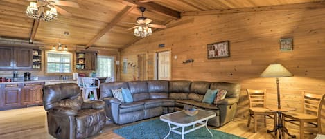 A cozy cabin interior with a wooden ceiling, leather recliner, sectional sofa, dining table, and chairs.
