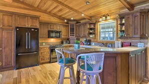 Une cuisine avec des meubles de rangement en bois, un réfrigérateur noir, un four à micro-ondes, une cuisinière et un coin repas comprenant deux chaises en osier et une table ronde.