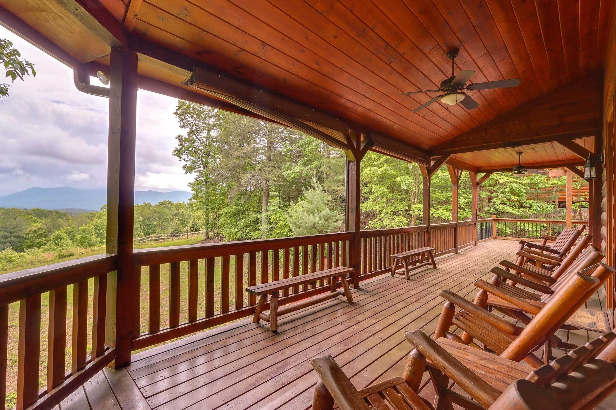 A wooden deck with benches and chairs, overlooking a lush landscape with trees and mountains.
