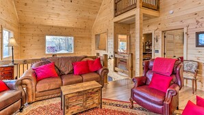 L’intérieur chaleureux d’un chalet avec un canapé en cuir, un fauteuil rouge et une table basse en bois.
