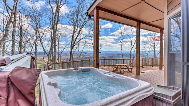 Un bain à remous sur une terrasse en bois, avec vue sur les montagnes et les arbres.