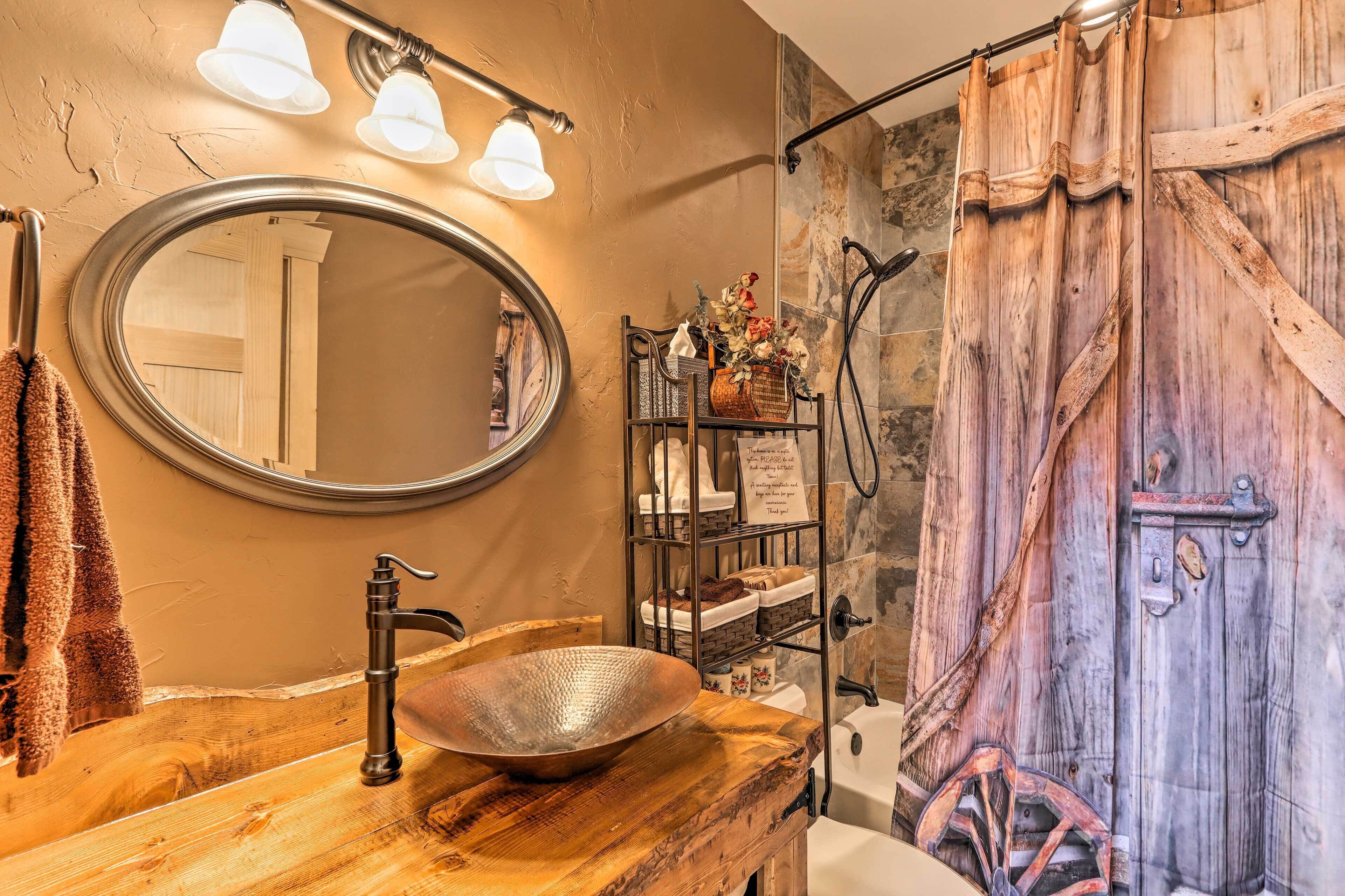 A bathroom with a wooden vanity, a round mirror, a vessel sink, and a shower curtain.
