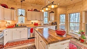 Une cuisine rustique, située dans une cabane en bois, avec des meubles blancs, un plan de travail en bois et un tapis rouge.