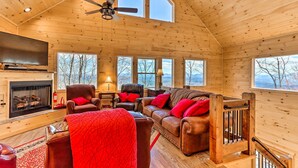 L’intérieur chaleureux d’un chalet en bois, avec une cheminée, des meubles en cuir et de grandes fenêtres donnant sur le paysage extérieur.