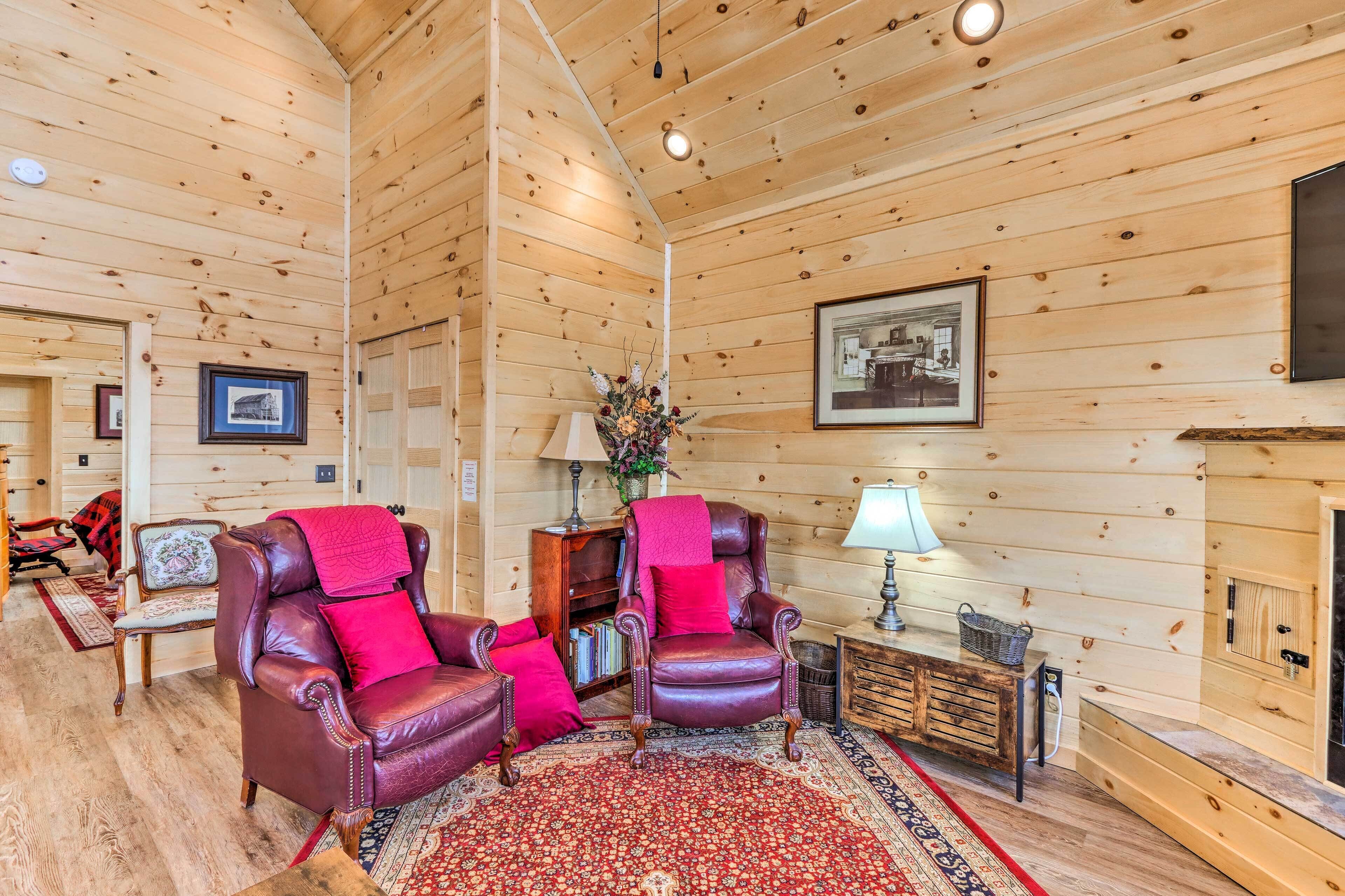 A cozy room with wooden walls, a fireplace, leather armchairs, a rug, and a bookshelf.