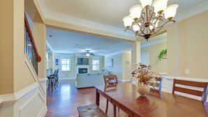 A spacious dining area with a wooden table and benches, a chandelier, and a view into a living room with a sofa and a kitchen in the background. - Spacious Kathleen Vacation Rental w/ Fireplace (Kathleen)
