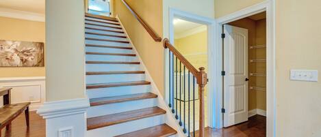 A staircase with wooden steps and a white handrail, leading to a room with a door and a light switch on the wall.