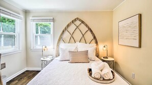 Een keurig opgemaakt slaapkamer met een bed, een hoofdeinde, nachtkastjes en een raam.