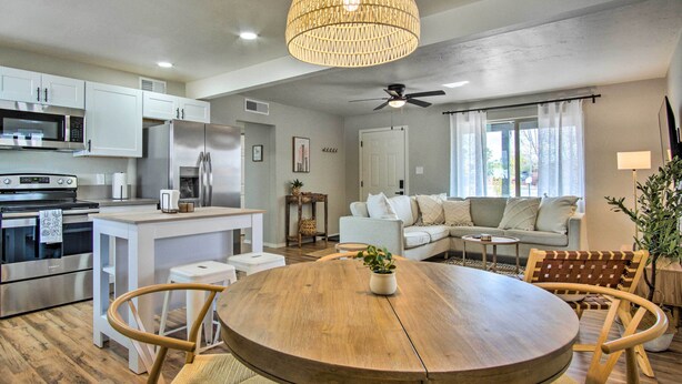 A modern kitchen with white cabinets, stainless steel appliances, and a wooden dining table with chairs. - Lovely Tucson Home ~ Walk to Reid Park Zoo! (Tucson)