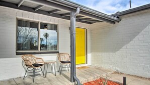 A building with a bright yellow door, a window with a view of palm trees, and two wicker chairs outside. - Lovely Tucson Home ~ Walk to Reid Park Zoo! (Tucson)