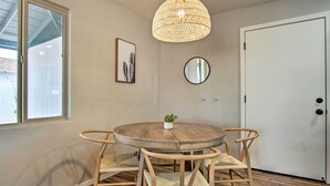 A round wooden table with four wicker chairs, a hanging woven light fixture, a small potted plant, a framed picture, and a round mirror on the wall. - Lovely Tucson Home ~ Walk to Reid Park Zoo! (Tucson)