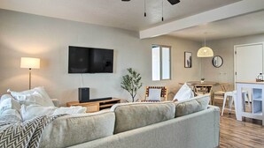A modern living room with a sofa, a TV mounted on the wall, a dining table with chairs, and a small kitchen area. - Lovely Tucson Home ~ Walk to Reid Park Zoo! (Tucson)