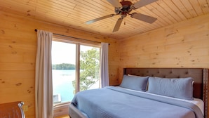 Camera da letto in una baita di legno, con un letto grande, una ventola a soffitto e una finestra con tende.