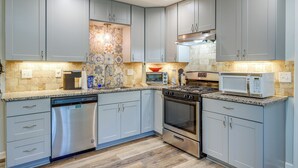 A modern kitchen with grey cabinets, stainless steel appliances, and a patterned backsplash.