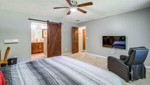 A bedroom with a bed, a ceiling fan, a TV, and a sliding door.