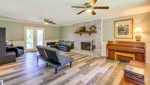 A living room with a fireplace, a piano, and a ceiling fan.
