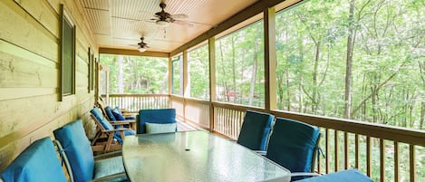 A covered outdoor seating area with a table and chairs, large windows, and a ceiling fan.